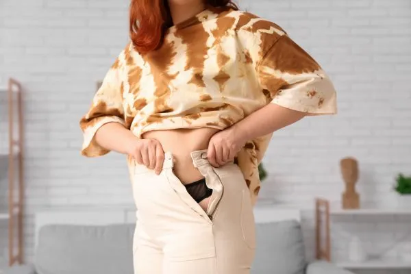 Image of woman trying to do her trousers up after pregnancy weight gain Little Bognor